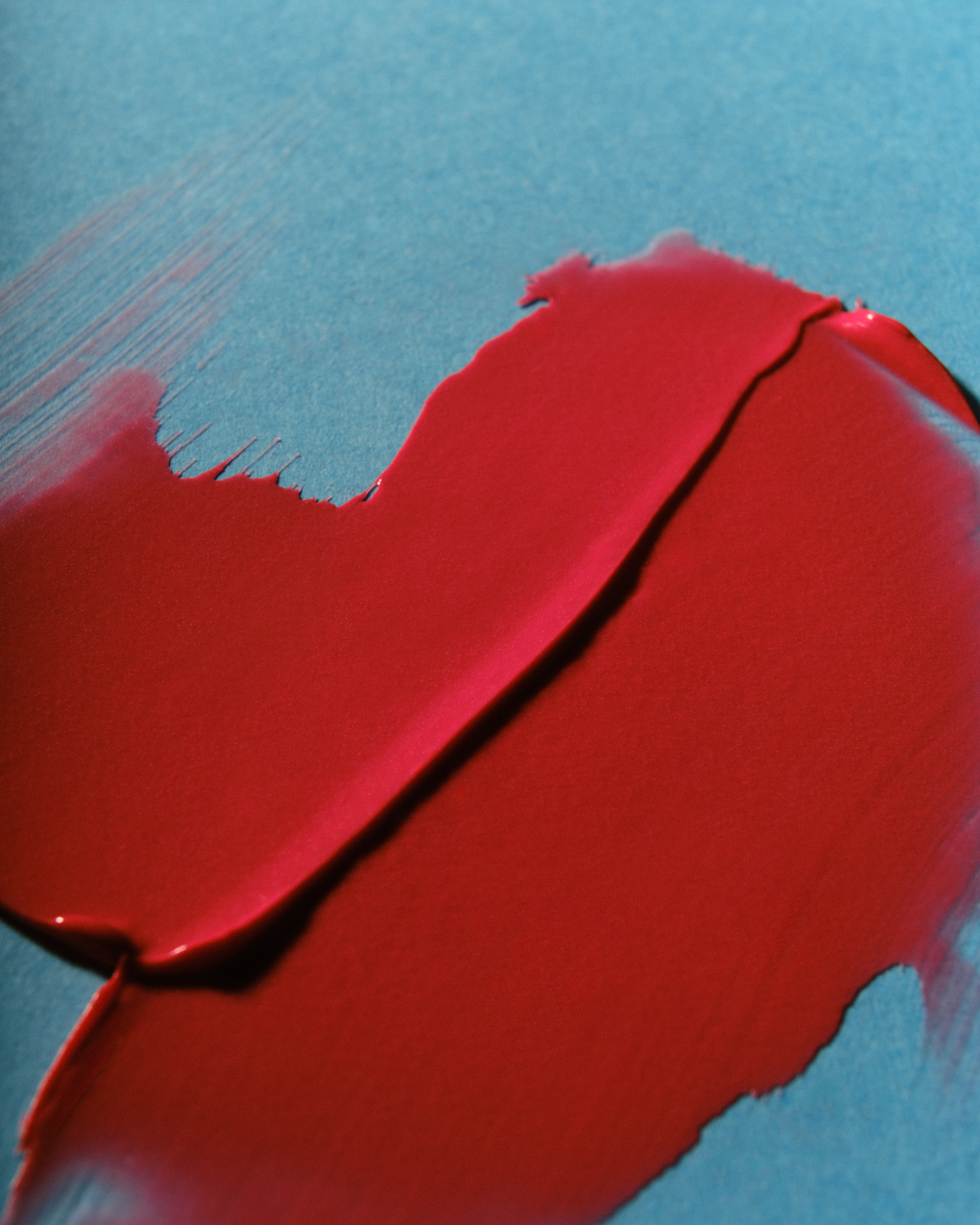 Aplatissements de texture cosmétique rouge, étalés sur un fond bleu pastel.