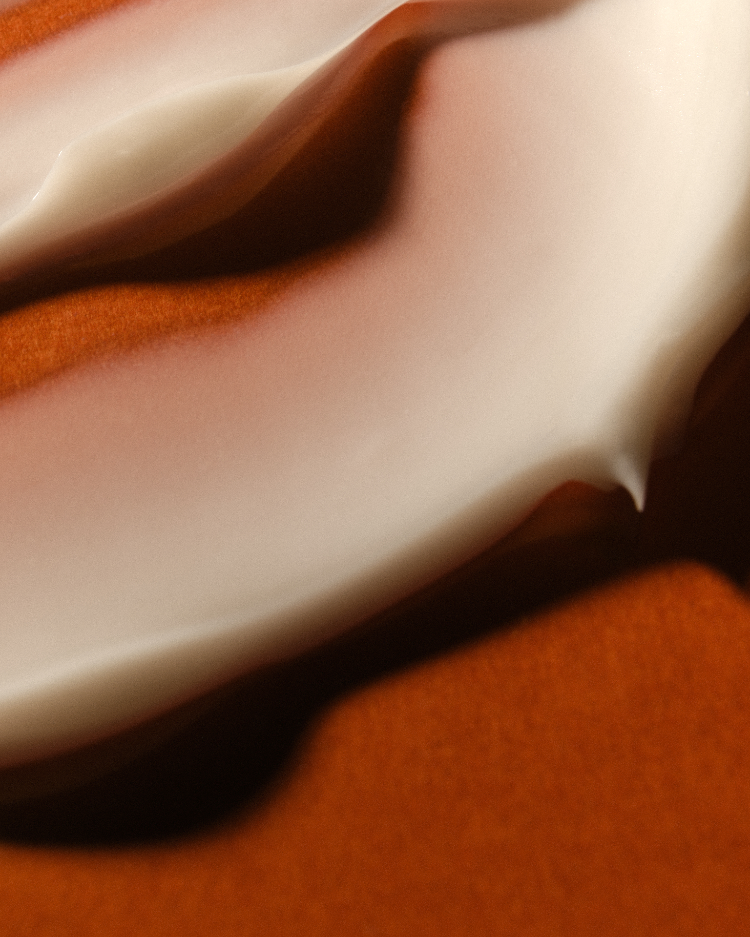 Empâtements de texture cosmétique blanche formant des courbes souples sur un fond brun.