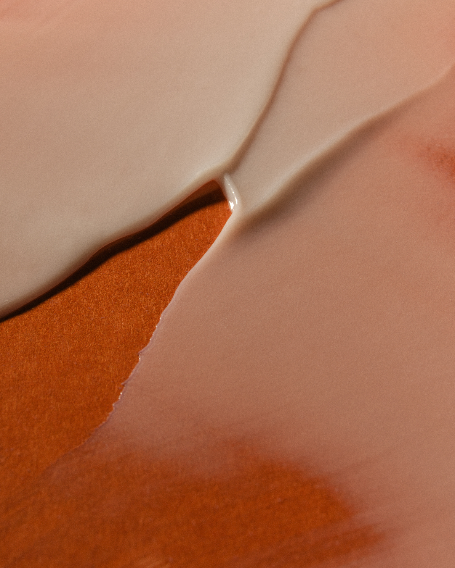 Étendue de texture cosmétique beige, appliquée en larges aplats sur un fond brun mat.