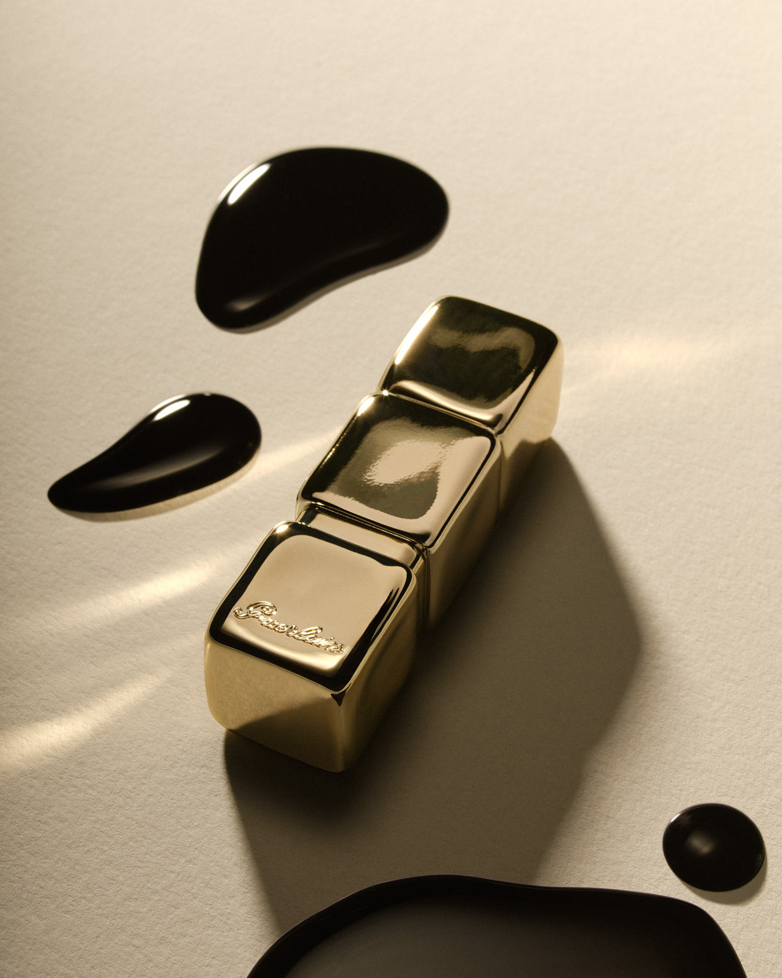 Étui cosmétique doré posé sur un fond beige, entouré de gouttes de texture humide noire.