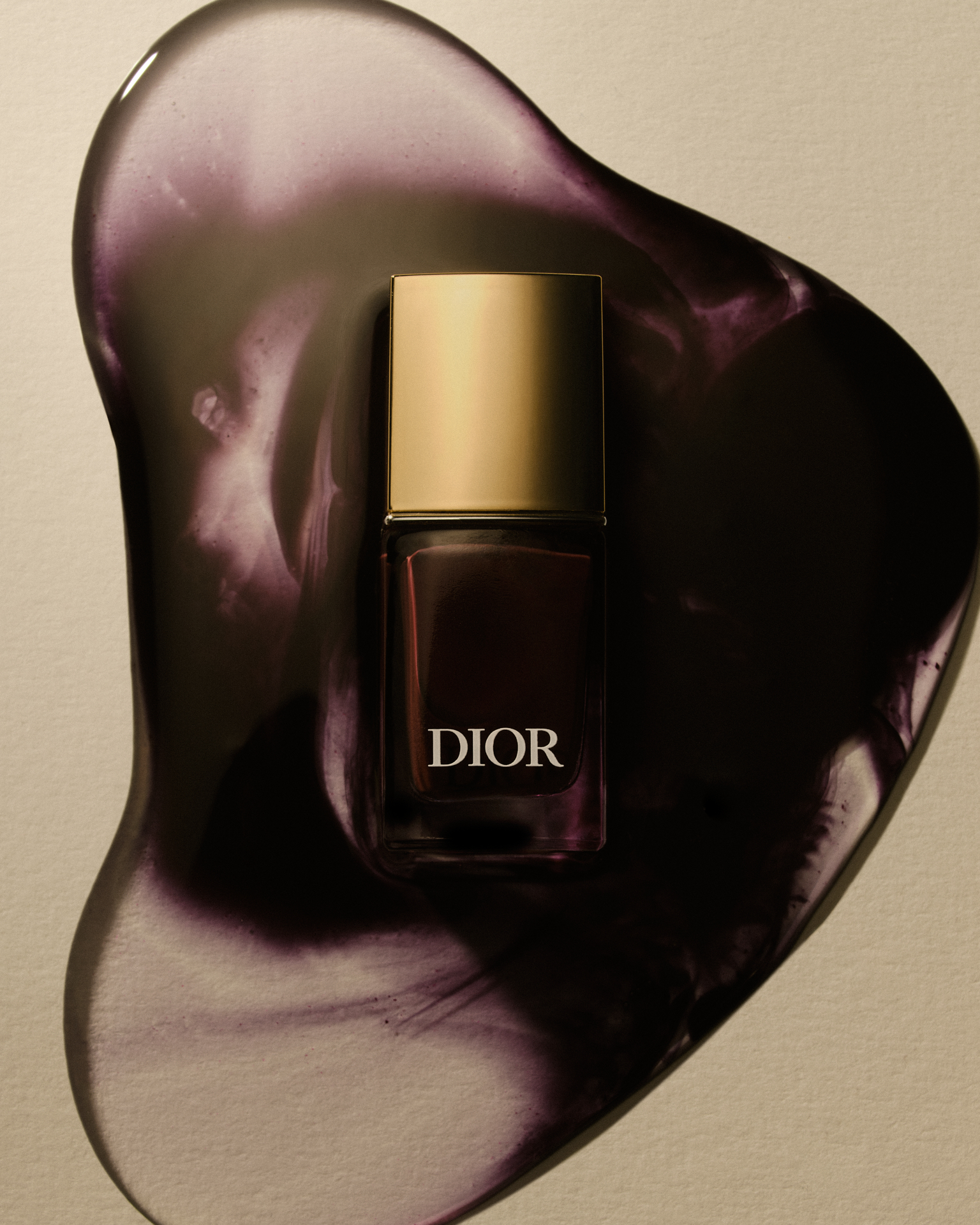 Flacon de vernis dior posé au centre d’une étendue de texture violette brillante sur un fond beige.